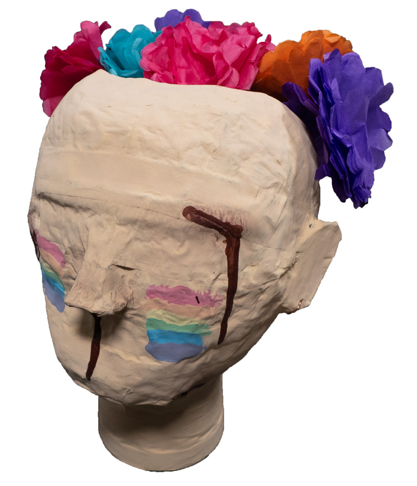 Paper Mache head with colorful flowers for hair, rainbow cheeks, and what appears to be blood dripping from the nose and eyebrow.