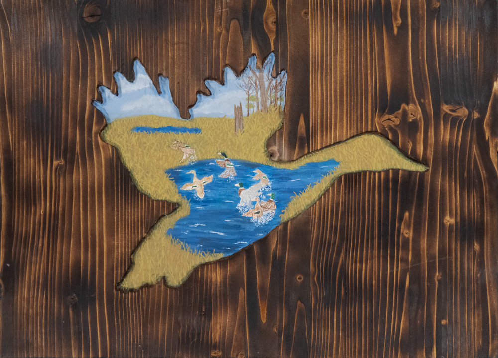 A painting of ducks in a pond appears in a duck-shaped recess into a wooden board that has been burned.